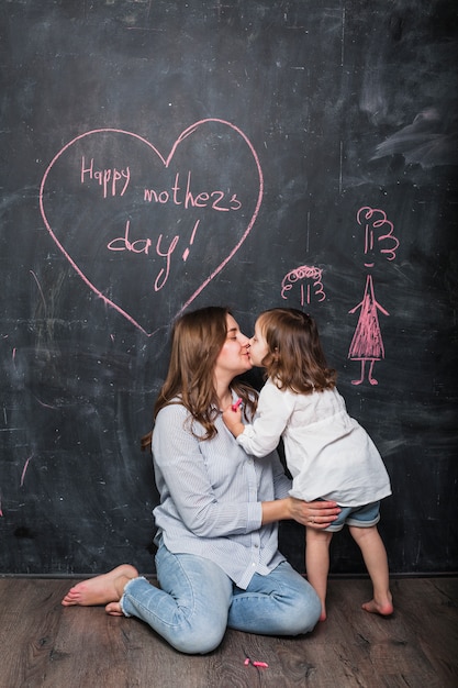 Free photo mother and daughter kissing near happy mothers day inscription