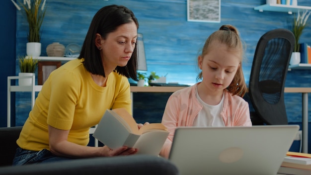 Free photo mother and daughter learning together with books and laptop for remote education. child using device to study for online courses and lessons. primary school girl studying with parent