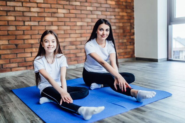 Mother and daughter practicing yoga in butterfly pose at home.. Health.