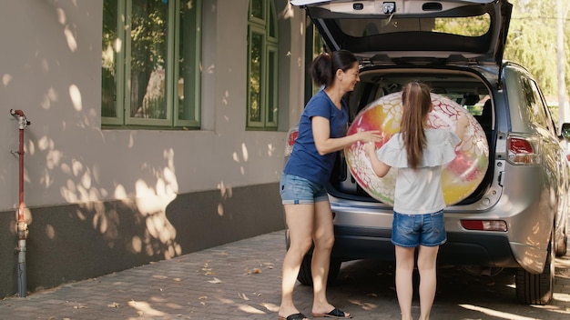 Free photo mother and daughter putting luggage in car trunk while enjoying holiday field trip. woman and little girl loading vehicle with luggage while getting ready for vacation citybreak.