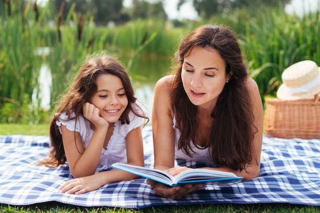 Free photo mother and daughter reading book outdoors