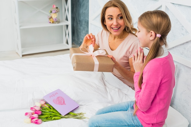 Free photo mother and daughter sitting on bed with gift