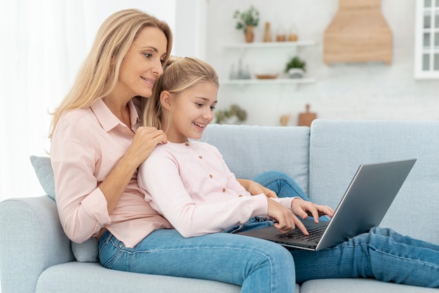 Mother and daughter sitting on sofa and working on laptop