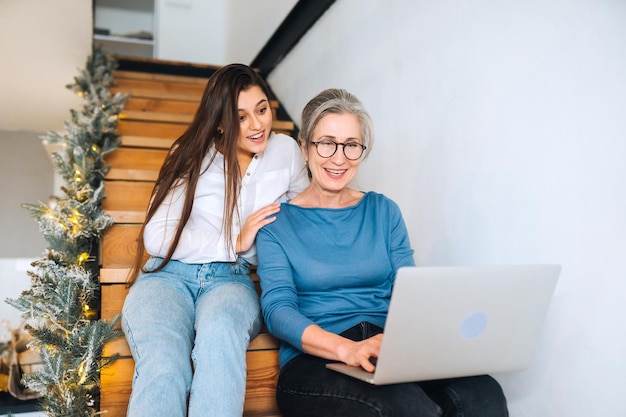 Mother and daughter sitting on the steps and watching something on laptop