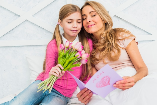 Mother and daughter sitting with flowers and greeting card 