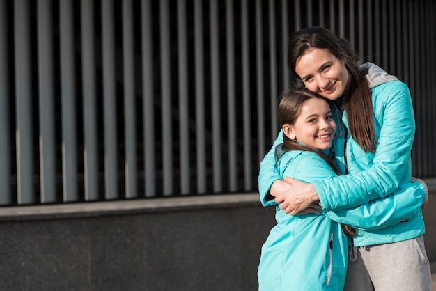 Mother and daughter in sportswear hugging with copy space