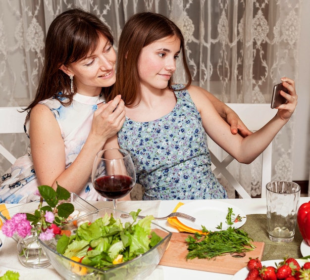 Mother and daughter taking selfie at dinner table