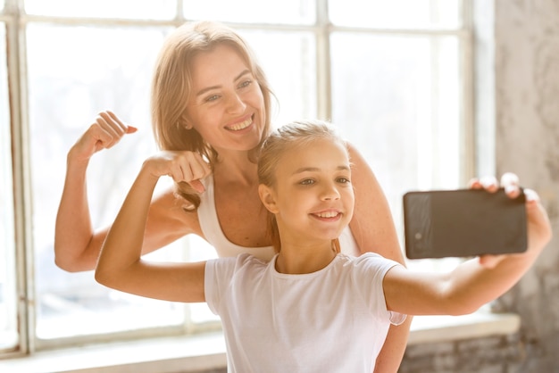 Free photo mother and daughter taking selfie flexing arm muscles