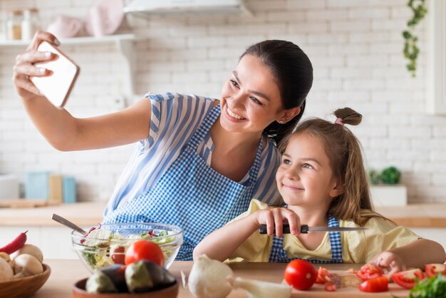 Mother and daughter taking selfie in kitchen