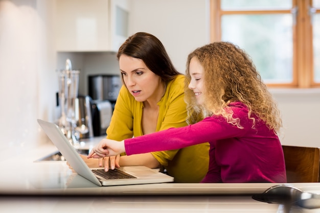 Mother and daughter using laptop in kitchen