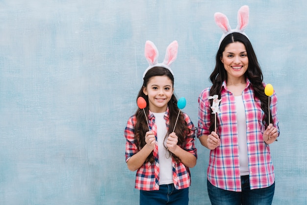 Mother and daughter wearing bunny ears holding easter eggs and bunny props