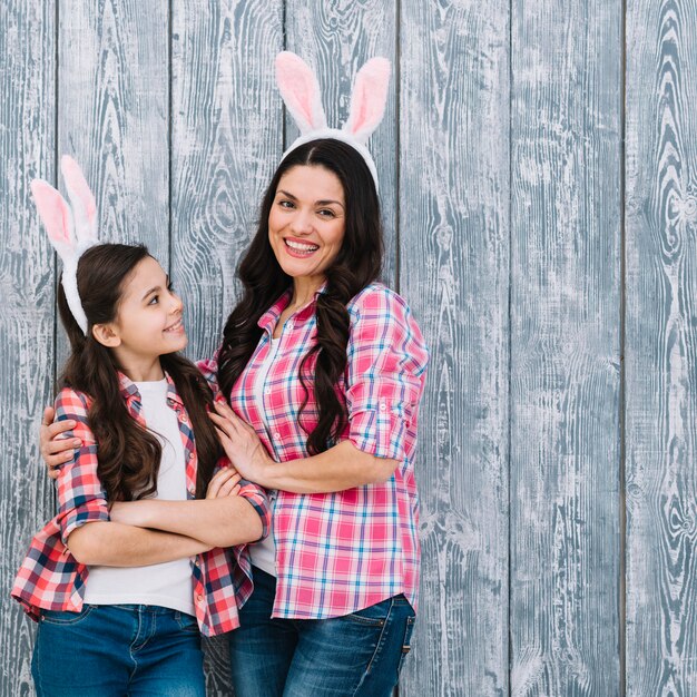 Mother embracing her pretty daughter wearing bunny ear's on gray wooden wall