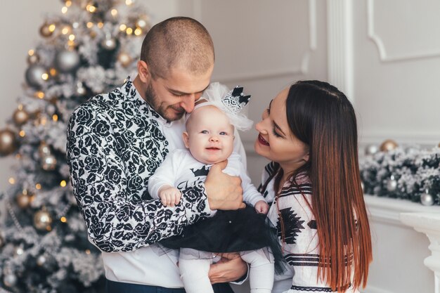 The mother and father embracing their daughter and standing near Christmas Tree