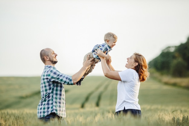 Free photo mother and father hold their son standing among the field