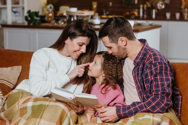 Mother and father reading book with daughter on the couch