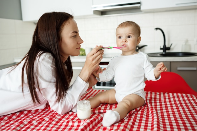 Mother feed cute baby yoghurt with spoon