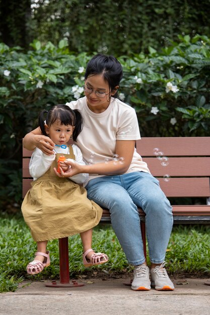 Mother and girl sitting on bench full shot