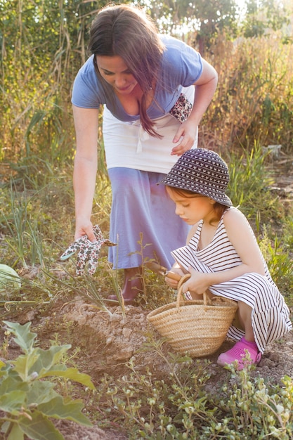 Free photo mother giving gloves to her daughter holding trowel sitting in field