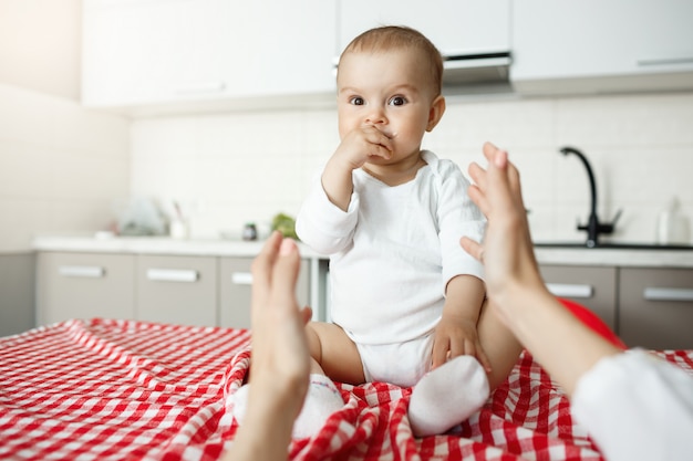 Mother hands reaching to her cute baby sitting on desk