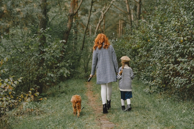 Mother and her daughter playing with dog. Family in autumn park. Pet, domestic animal and lifestyle concept. Autumn time.