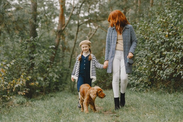 Mother and her daughter playing with dog. Family in autumn park. Pet, domestic animal and lifestyle concept. Autumn time.