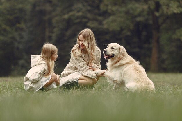 Mother and her daughter playing with dog. Family in autumn park. Pet, domestic animal and lifestyle concept