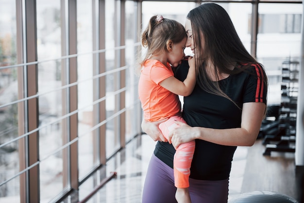 Mother holds her daughter in her arms in the gym.