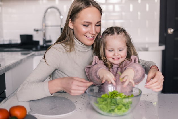 Mother and little girl slicing vegetables in the kitchen preparing a salad