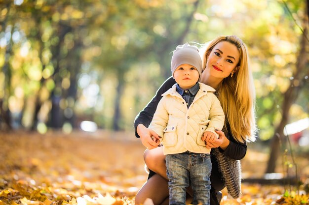 Mother and little son in park or forest, outdoors. Hugging and having fun together in autumn park