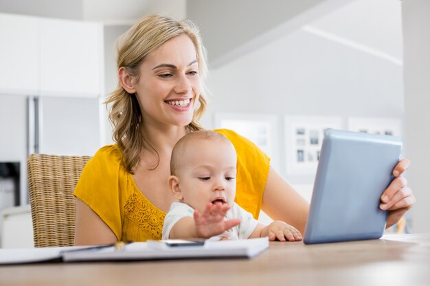 Mother looking at digital tablet with baby boy in kitchen