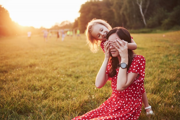 Mother plays with her daughter on the street in the park at sunset