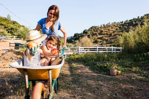 Free photo mother pushing her daughters in wheelbarrow at field