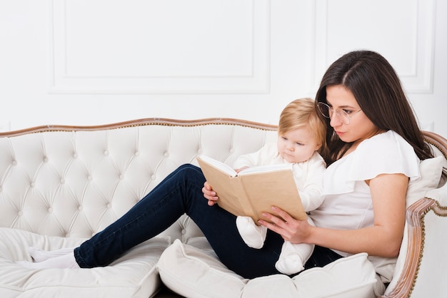 Free photo mother reading on sofa with baby