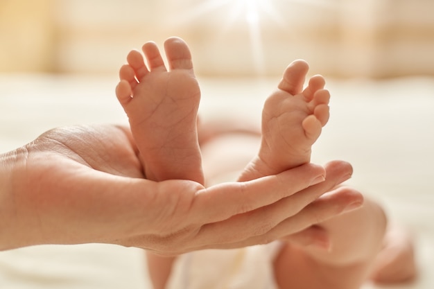 Free photo mother's hand holding newborn baby's barefoot, mommy making massage for infant for normalization of the nervous system and development of coordination of movements.