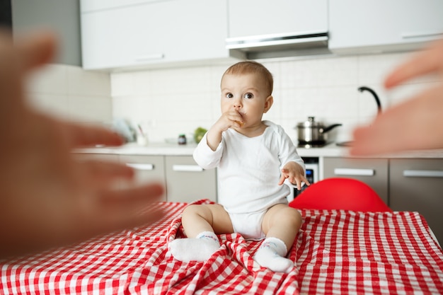 Mother's hands reaching to take cute baby sitting kitchen table