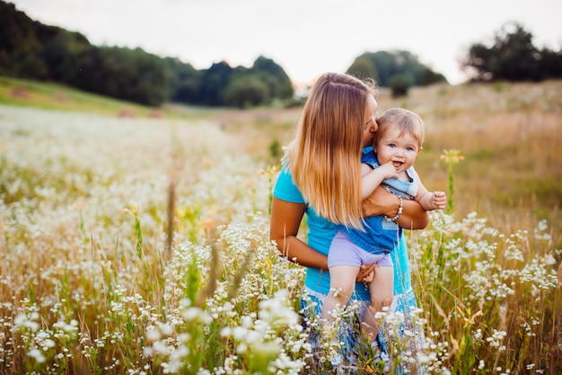 Mother stands with a child on the field with white flowers 