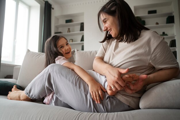 Mother tickling kid on couch full shot