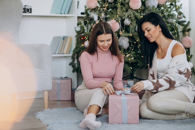 Mother with adult daughter with christmas presents by christmas tree