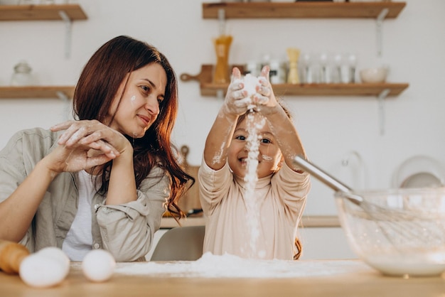 Mother with daughter playing with flour and baking at kitchen