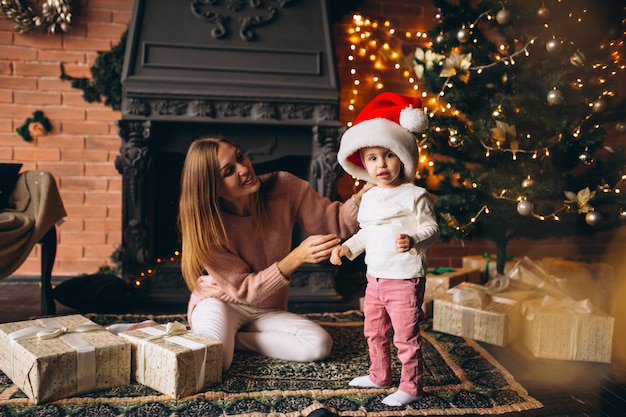 Mother with daughter sitting by Christmas tree