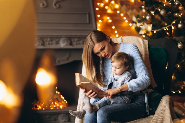 Mother with daughter sitting in chair by Christmas tree