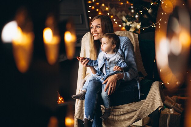 Mother with daughter sitting in chair by Christmas tree