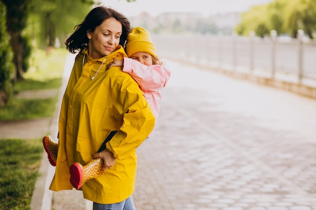 Mother with daughter walking in park in the rain wearing rubber boots