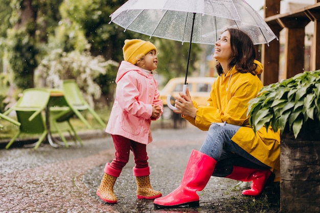 Mother with daughter walking in park in the rain wearing rubber boots