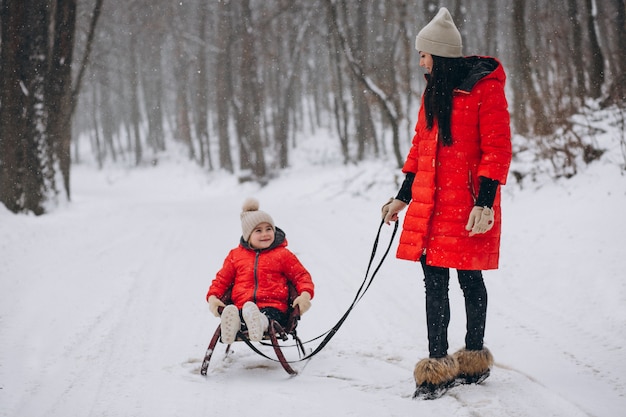 Mother with daughter in winter park sledging