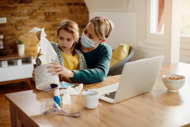 Mother with face mask giving a box of tissues to her small daughter at home