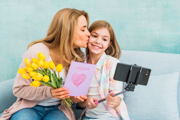 Free photo mother with gifts kissing daughter taking selfie