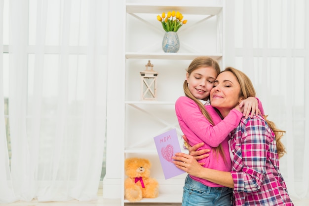 Mother with greeting card hugging daughter 