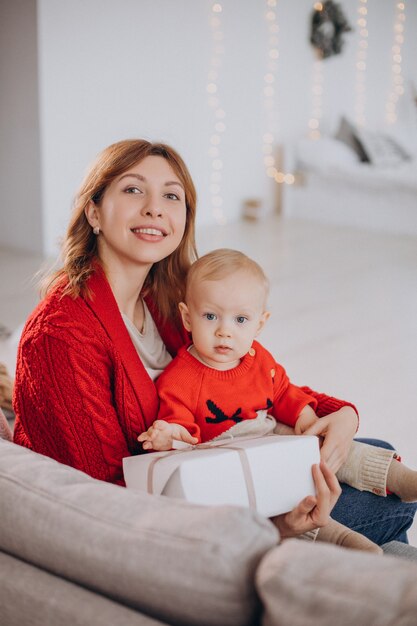 Mother with her baby son sitting on sofa and unpacking christmas presents