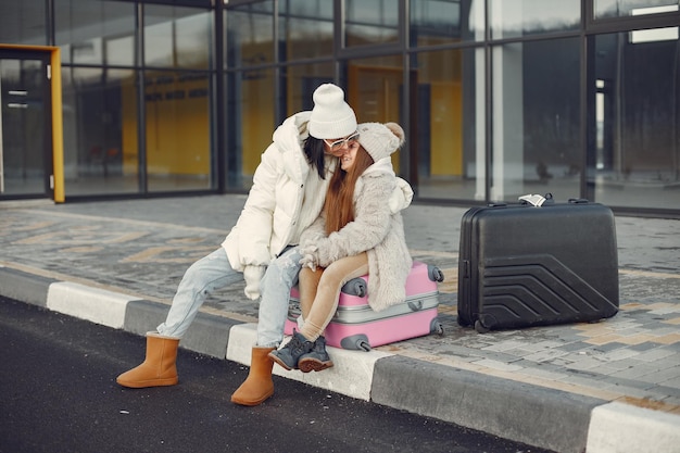 Free photo mother with her daughter sitting outdoors on a luggage and waiting for travel